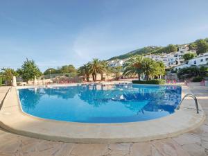 a large blue swimming pool with palm trees and buildings at 6 persoons bungalow met gemeenschapelijk zwembad in Benitachell