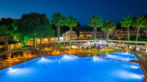 a large pool with chairs and palm trees at night at Lykia Botanika Beach Fun & Club - All Inclusive in Fethiye