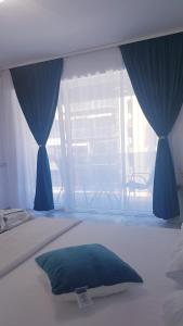 a bedroom with a bed with blue curtains and a window at Garsoniera Camy in Saturn