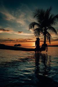 dwoje ludzi siedzących pod palmą na plaży w obiekcie Nyande Raja Ampat w mieście Pulau Mansuar