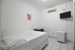 a white bedroom with a bed and a tv at Hotel Tapajós in Cuiabá
