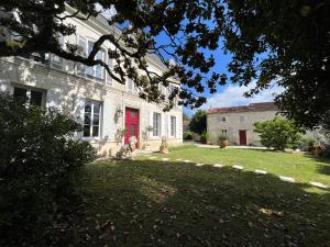 a white house with a red door and a yard at Chambres d'hôtes dans Maison de maître in Chaniers
