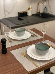 a table with two bowls and plates and wine glasses at Apartman Vasia Subotica in Subotica
