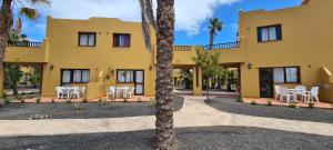 żółty dom z białymi krzesłami i palmą w obiekcie Beautiful garden flat nearly refurbished free WiFi w Corralejo