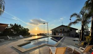 uma piscina com cadeiras e um pôr-do-sol ao fundo em VILLA PANORAMICA DELL'ETNA em SantʼAlfio