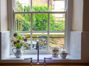 a kitchen window with a sink and flowers on a counter at Woodside Cottage in Snainton