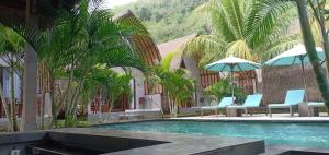 a swimming pool with chairs and umbrellas and palm trees at Bale Lumbung Bungalows in Nusa Penida