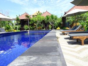 a pool at a resort with benches and umbrellas at Perdana Homestay Lembongan in Nusa Lembongan