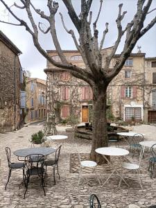 un patio con mesas, sillas y un árbol en Entre Terre et Ciel. en Saignon