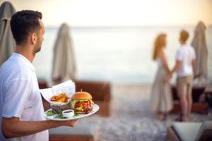 un hombre sosteniendo un plato con un sándwich y papas fritas en Valtos Beach Hotel, en Parga