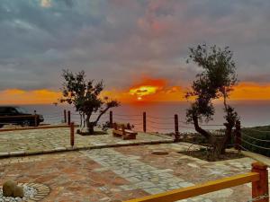a sunset over the ocean with a fence and trees at Rahoni Park & Suites in Dhërmi