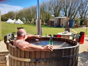 a man sitting in a hot tub with a bottle at Angela's Rest Shepherds Hut with Scandi Hot Tub in Boston