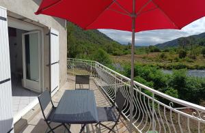 une terrasse avec un parasol rouge, une table et des chaises dans l'établissement Gite de POUNARD bord de rivière plage privée, 