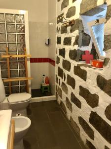 a bathroom with a toilet and a stone wall at Casa Auri in Faial da Terra
