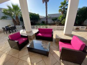 un patio con sillas rosas, mesas y palmeras en Sabea Guest House, en Melissano