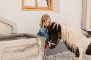 mała dziewczynka stojąca obok konia i patrząca na koryto w obiekcie Gut Berg Naturhotel w mieście Sankt Johann im Pongau