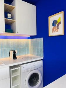 une machine à laver dans une cuisine avec un mur bleu dans l'établissement Flore, au Grau-du-Roi