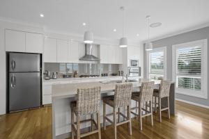 a kitchen with white cabinets and a large island with bar stools at Little Lake Beach House - Beachside 4 Bedroom Luxury Home in Lake Illawarra