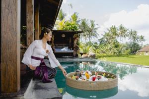 a woman standing next to a pool with a basket of food at Airsania Ubud Antique Villas in Ubud