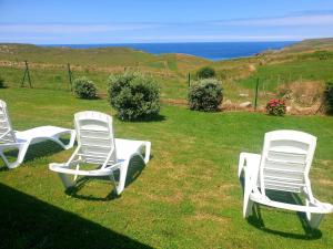 drie witte stoelen in het gras bij de oceaan bij Apartamentos Santa Justa in Ubiarco