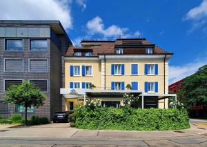 ein gelbes Gebäude mit blauen Fenstern auf einer Straße in der Unterkunft Hotel Zugertor in Zug