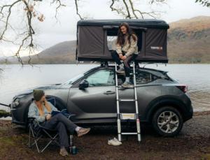 a woman sitting on the roof of a car with a camper at Hexham Tentbox Hire in Hexham