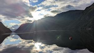a reflection of the sun in the water with mountains at Frafjord Apartments Thor in Dirdal