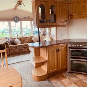 a kitchen with wooden cabinets and a living room at 157 Amour Caravan in Tywyn