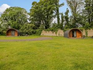 two huts in a field with trees in the background at Pod 1 in Seascale