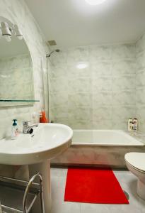 uma casa de banho com um lavatório branco, uma banheira e um tapete vermelho em Tu hogar en el corazón de O Salnés em Meaño