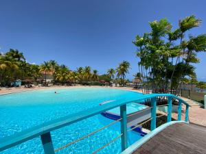 une grande piscine bordée de palmiers et une plage dans l'établissement Tucum Home - Appart au Village Vacances Sainte Anne, à Sainte-Anne