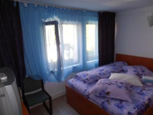 a bedroom with a bed and a chair with blue curtains at Pensiunea Sans Rival in Iaşi