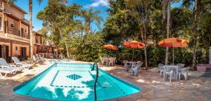 a swimming pool with tables and chairs and umbrellas at Pousada Y-Goá in Bertioga