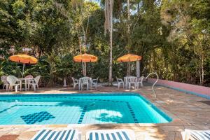 a swimming pool with tables and chairs and umbrellas at Pousada Y-Goá in Bertioga