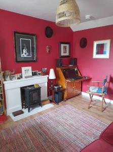 a living room with a red wall with a fireplace and a piano at Gunn Croft in Balallan