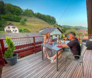 Un uomo e una donna seduti a un tavolo su un ponte di Gîte du Silberwald charmant gîte avec spa - jacuzzi , accès privatif a Stosswihr