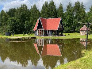 a house with a red roof sitting on top of a lake at Sodyba Anykščių raj. in Anykščiai