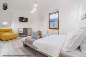 a white bedroom with a bed and a yellow chair at Sierra - Northstar Apartments in Braşov