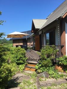 ein Haus mit einer Holzveranda und einem Sonnenschirm in der Unterkunft 八ヶ岳 HOKUTO BASE -Yatsugatake- in Hokuto