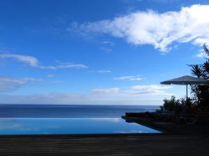 a swimming pool with an umbrella and the ocean at Casa do Lado in Povoação