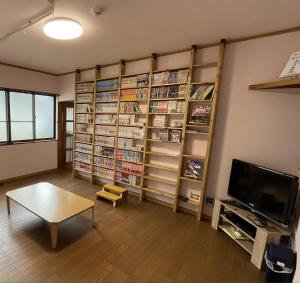 ゲストハウス　鍼灸院　boshcetto في يوشينو: غرفة بها رفوف كتاب وتلفزيون وطاولة
