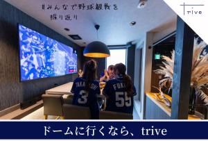 two girls in jerseys sitting at a table watching a television at trive ozone バンテリンドーム ナゴヤ近く 都心部好アクセス 大曽根駅 徒歩3分 in Nagoya