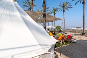 a tent on the beach with chairs and palm trees at Mia Glamping Kinneret in HaOn