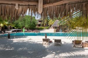 a beach area with a pool, chairs, and a beach umbrella at Mwezi Boutique Resort in Jambiani