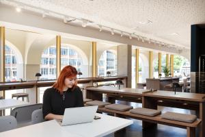 a woman sitting at a table with a laptop at MEININGER Hotel Bremen Hauptbahnhof in Bremen