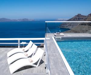 a pool with white lounge chairs and the ocean at Hotel Thireas in Fira