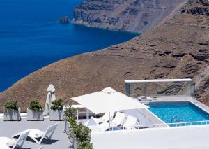 a pool with chairs and an umbrella and the ocean at Hotel Thireas in Fira