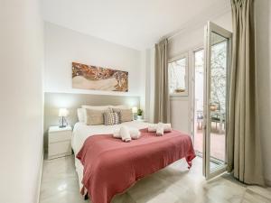 a white bedroom with a large bed with a red blanket at San Marcos Apartamentos in Seville
