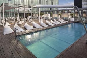 - une grande piscine avec des chaises blanches dans un bâtiment dans l'établissement The Level at Melia Barcelona Sky, à Barcelone