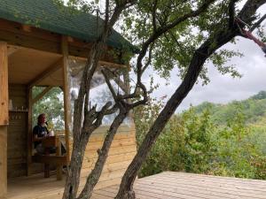 Una donna seduta a un tavolo sul ponte di una casa sull'albero di Cabane Bivouac avec échelle à l'ombre des chênes a Idrac-Respailles